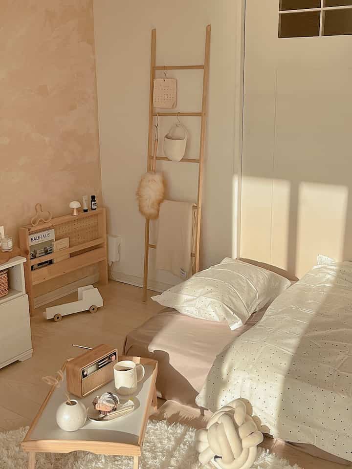 A beige and white toned studio apartment living room featuring a floor mattress and wooden furniture in a natural style