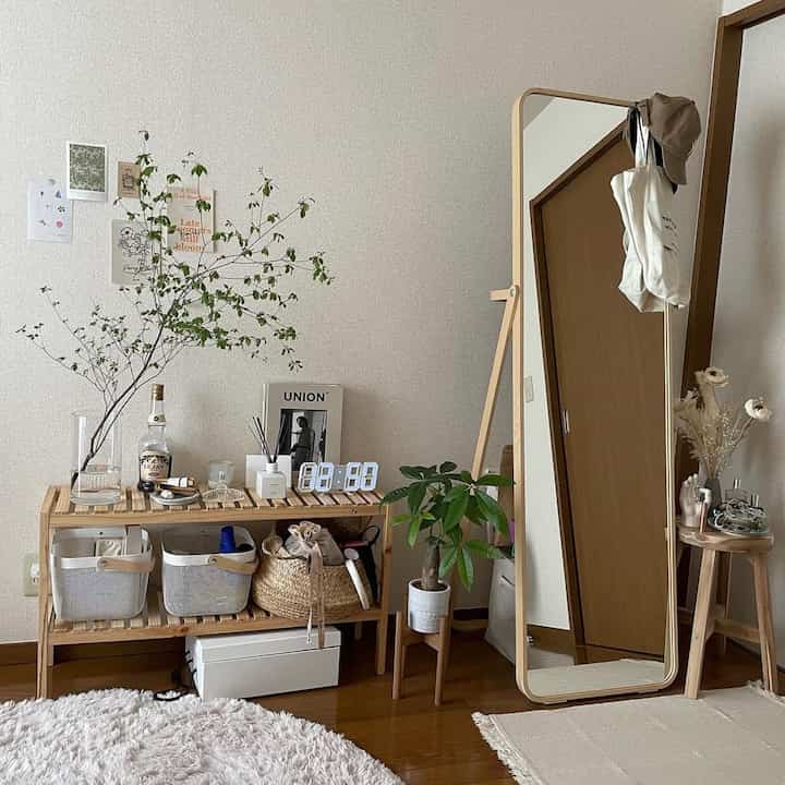 Natural wood-toned living space featuring a tall full-length mirror, wooden shelving with decor, and green plants in a simple setup