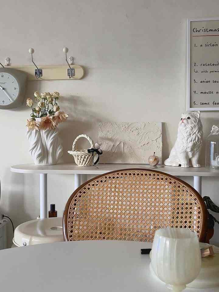 ナチュラルなベージュ色調のリビング、ラタンチェアとホワイトのコンソール棚に花瓶と猫のオブジェが配置された雰囲気のある空間