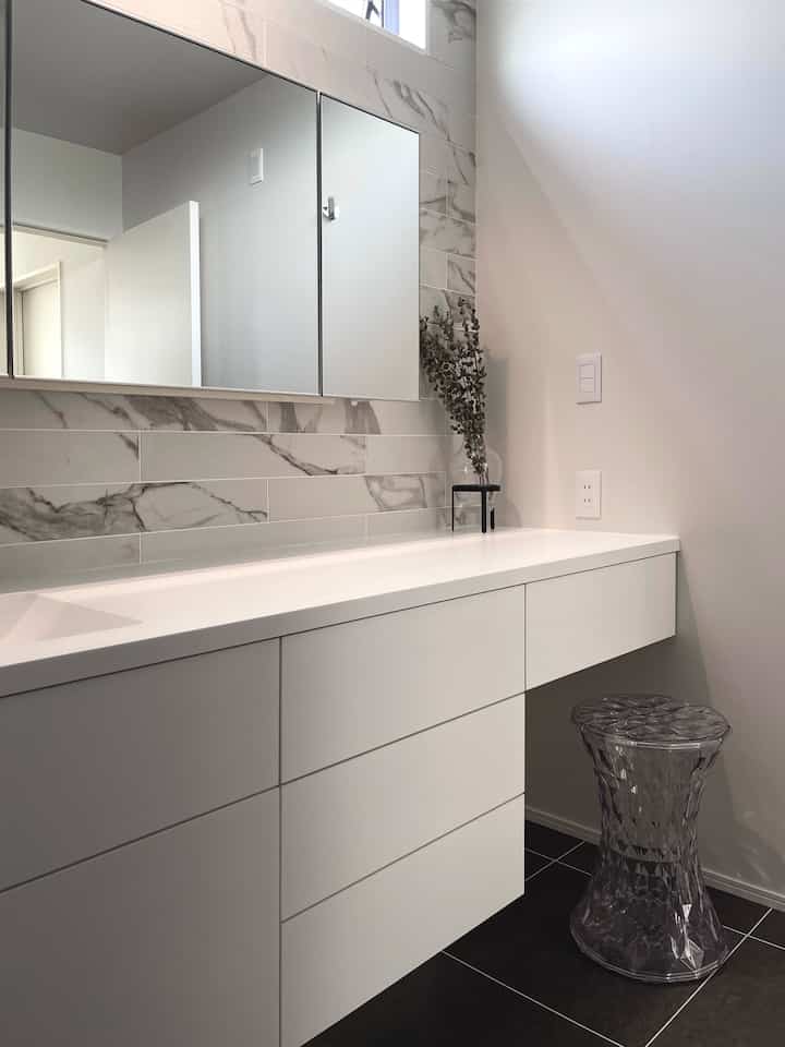 白と黒を基調としたバスルームのパウダールーム、収納キャビネットと透明なスツールが配置されたモダンで清潔感のあるインテリア