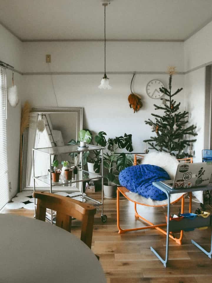 木目調の床と植物が調和した空間、シルバーのトローリーとオレンジのソファが配置されたナチュラルな雰囲気のお手洗い