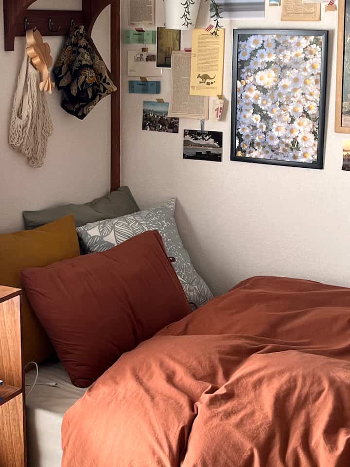 Warm brown-toned bedroom featuring a bed with multiple pillows and a daisy flower poster on the wall, creating a cozy atmosphere
