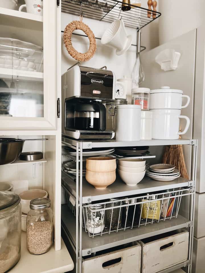 白とナチュラルな色調のキッチン、金属棚にコーヒーマシンや調理器具が整然と並べられた、雰囲気のあるおうちカフェ空間