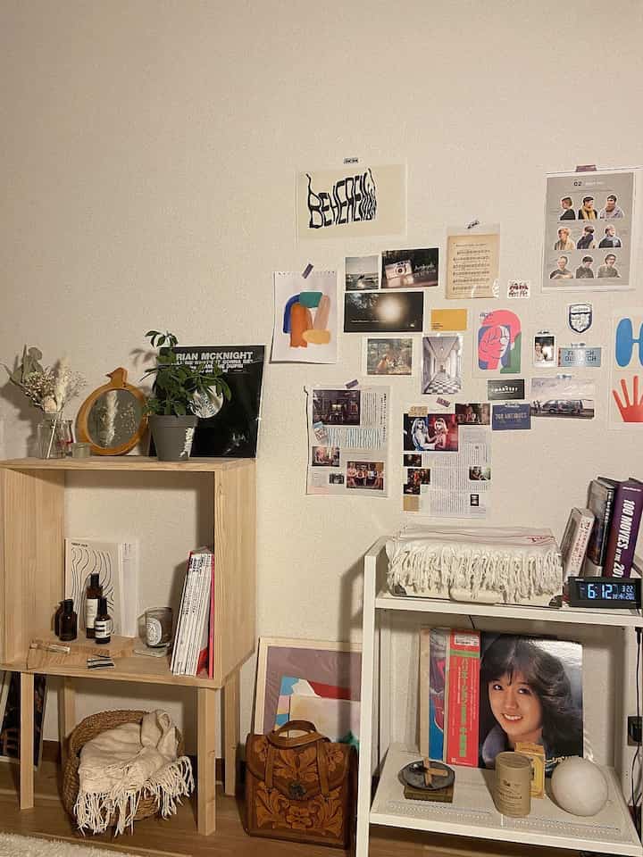 Bright natural-toned living room featuring a wooden bookshelf and diverse wall posters in a simple arrangement