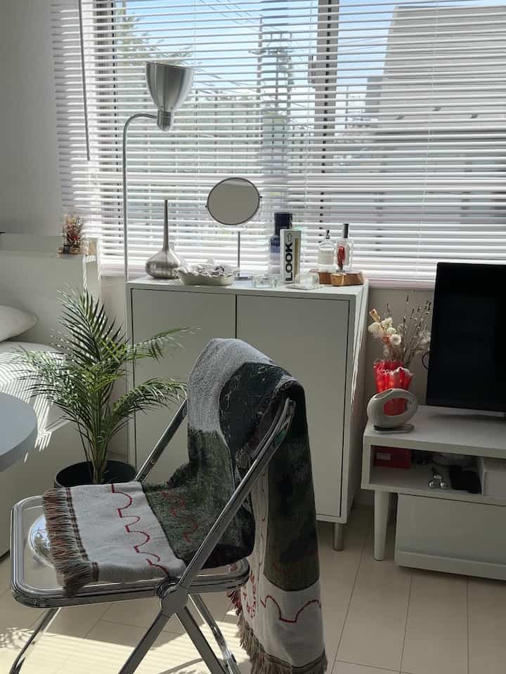 白と透明の素材が調和するリビング、折りたたみチェアと植物が配されたモダンで清潔感のある空間