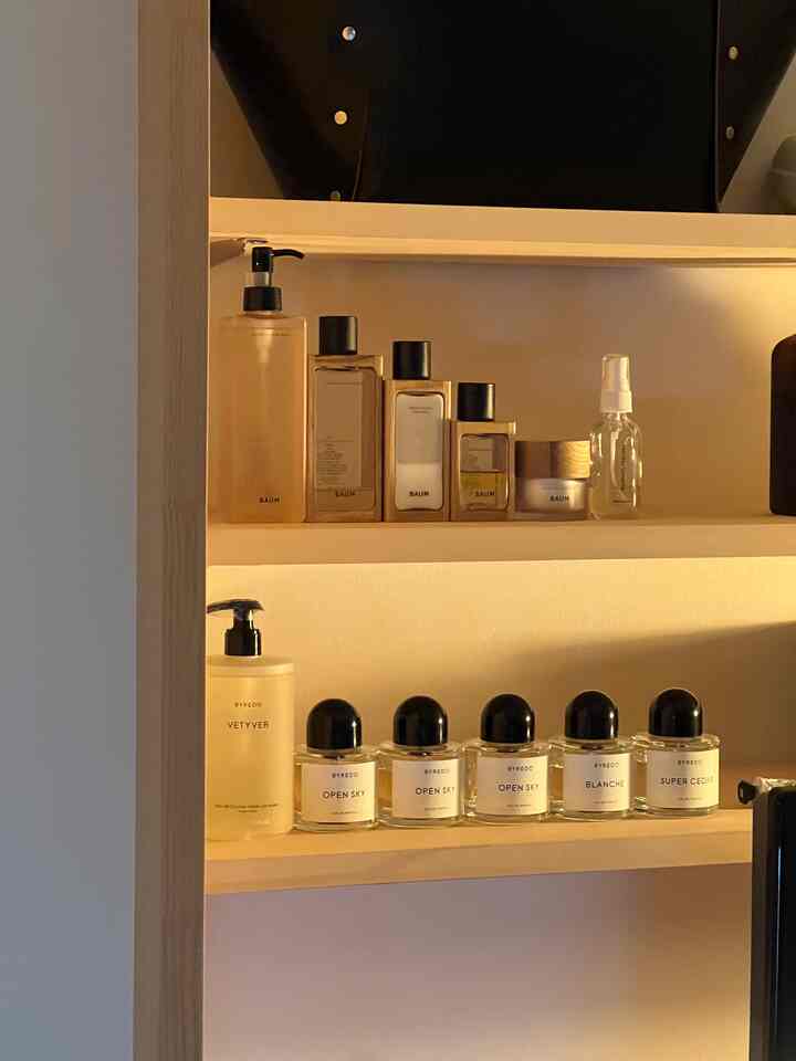 ナチュラルトーンのウッドシェルフに並べられたBAUMとBYREDOのスキンケアと香水が配置されたシンプルな化粧台の空間