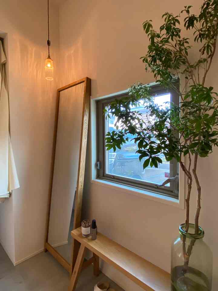 ナチュラルな木目調とネイビーの窓が調和した玄関、ペンダントライトと大きな植物のある雰囲気のあるインテリア