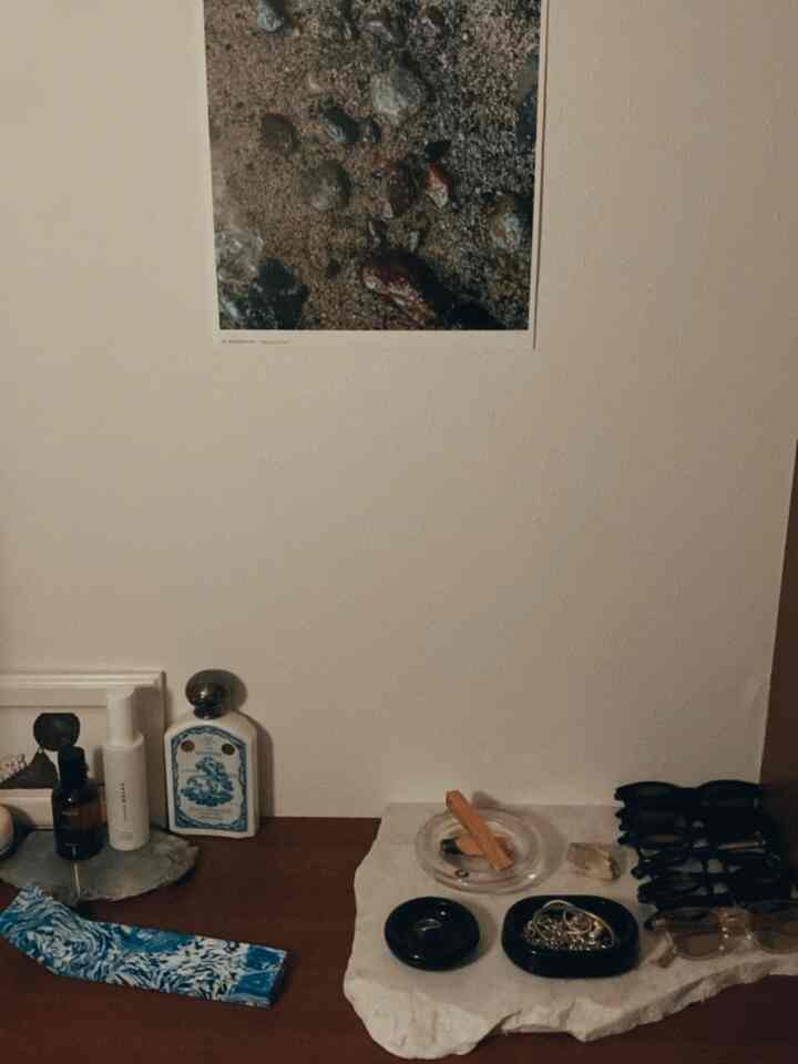 White-walled entrance table corner with brown wood surface, featuring neatly arranged glasses, rings, and perfume items