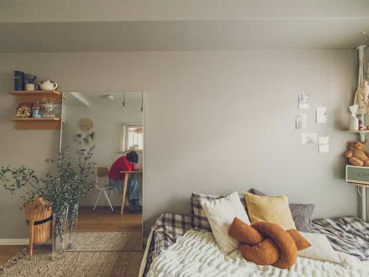 Beige and white toned bedroom with sofa bed featuring multiple cushions, showcasing a cozy natural modern interior style