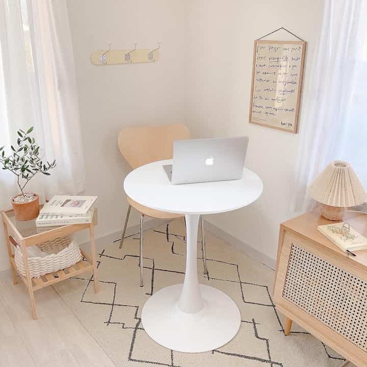A white and wood tone 6-tatami home office featuring a round desk with laptop, simple natural rug, and cozy decor elements