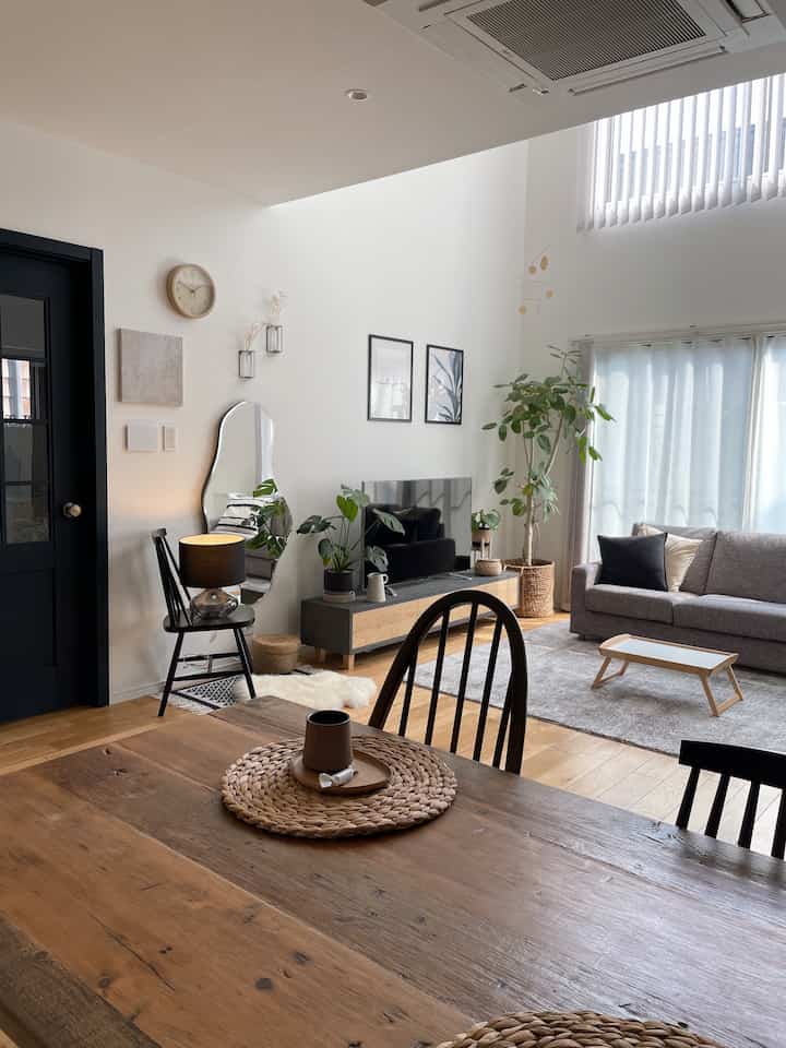 Natural-toned living room featuring a gray sofa, wooden dining table, plants, and rattan accents creating a warm atmosphere