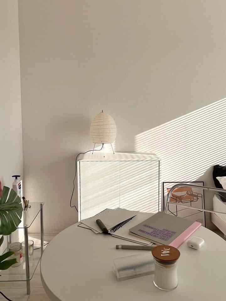 Bright natural-tone living room featuring round white table, simple storage cabinet, and warm natural light creating cozy atmosphere