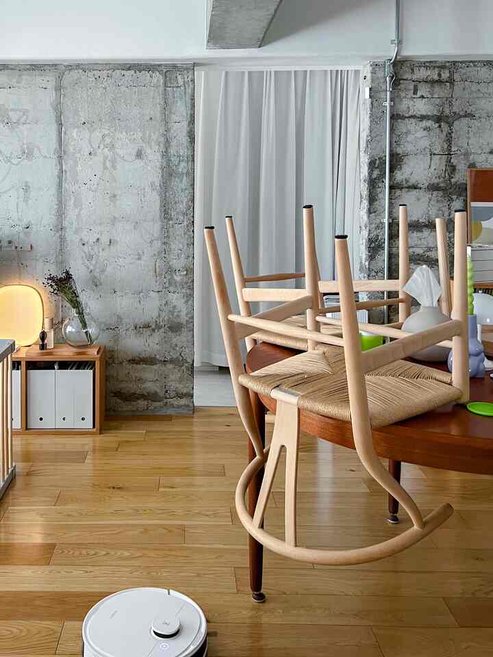 ナチュラルな木目調とコンクリート壁のリビング、カールハンセン＆サンの椅子とロボット掃除機が配置された雰囲気のある空間