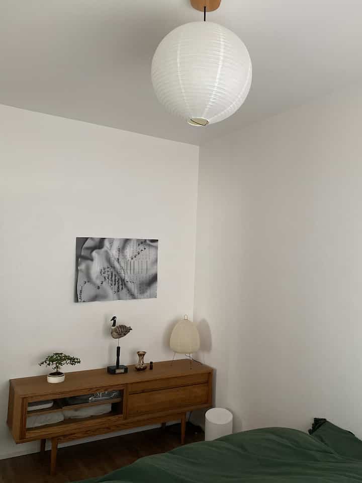 Bedroom with white walls and wooden dresser, featuring a moss green duvet cover, showcasing a simple and natural atmosphere