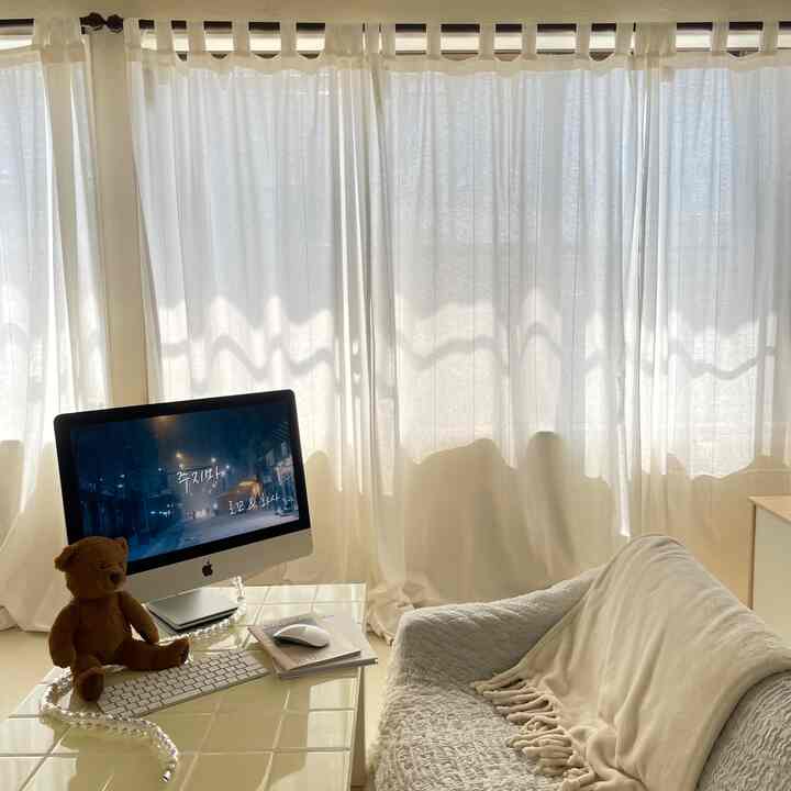 明るくアイボリー調のワンルームリビング、iMacのコンピューターとテディベアが置かれたコンパクトなホームオフィス空間