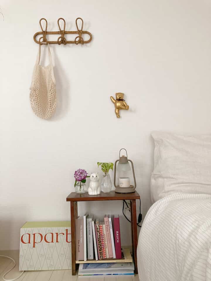 白と木目調の調和が感じられる寝室、ベッド脇の小さなナイトテーブルに花瓶と猫型のオブジェが配置されたシンプルなインテリア