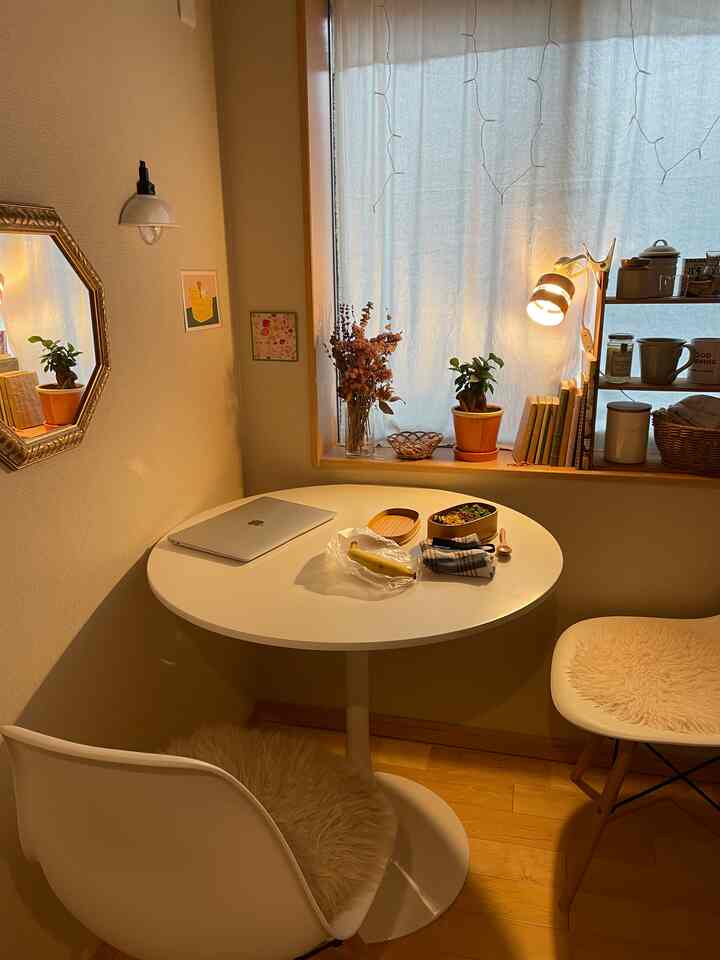 White and wood-toned cafe style studio apartment dining area featuring a round table, warm lighting, and cozy decorative elements