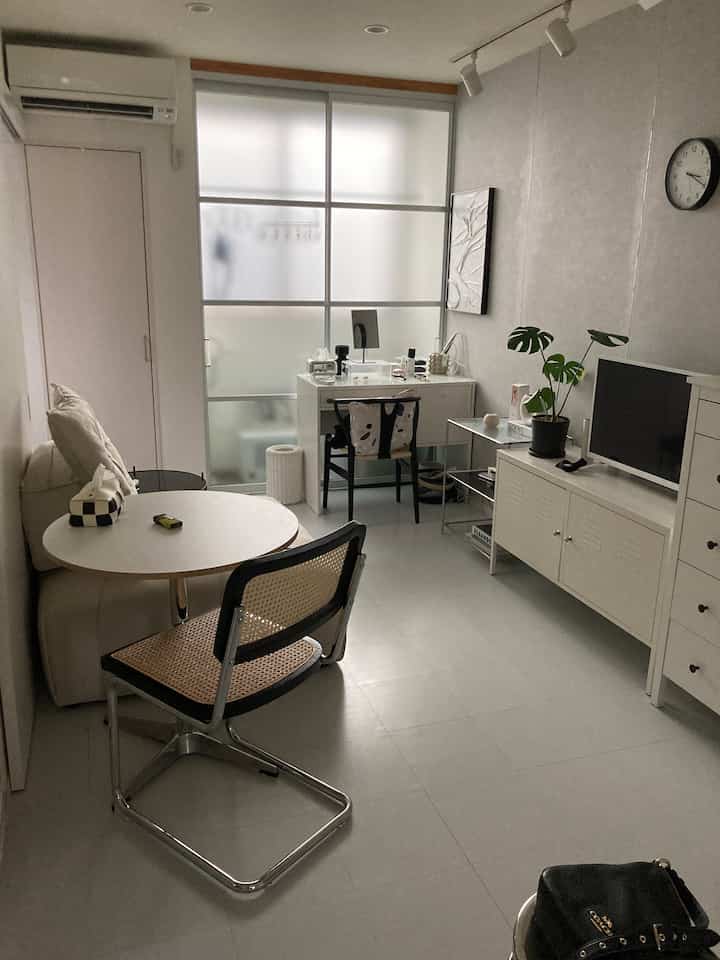 白を基調としたシンプルな一人暮らし用リビング、コンパクトな空間にテーブルとラタンチェアが配置された落ち着いたインテリア