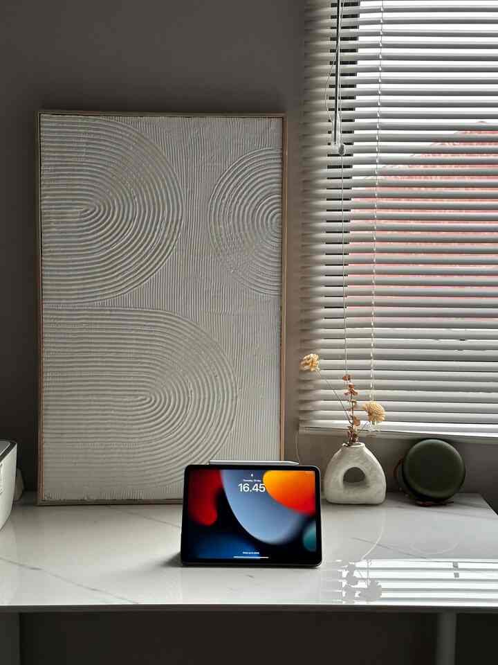 White and beige-toned entrance space featuring textured wall decor, tablet, and a minimalist clean desk arrangement