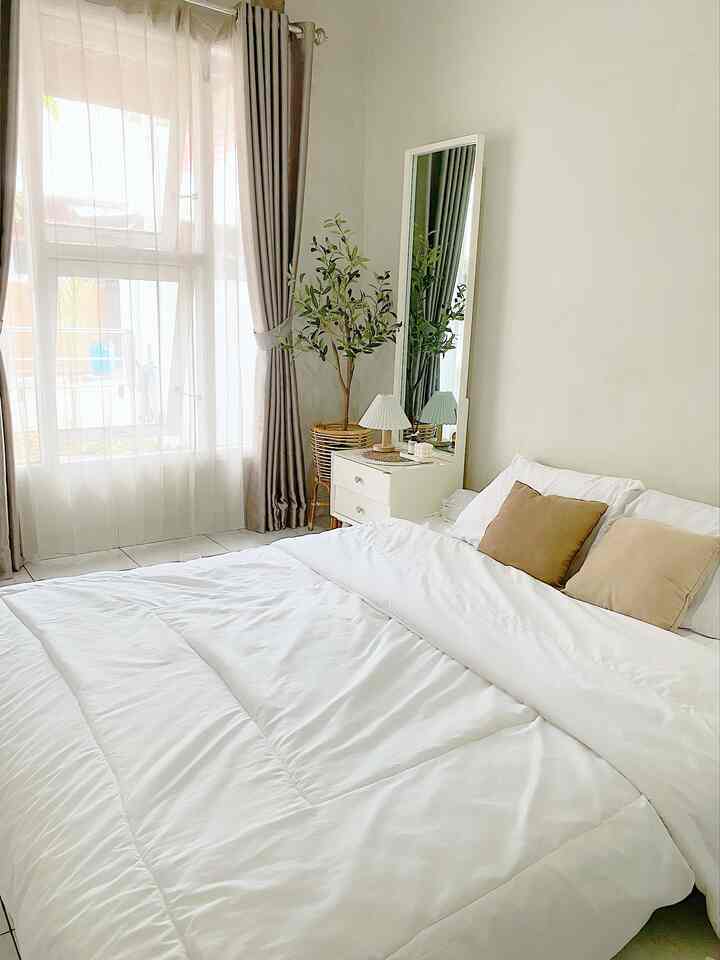 White and beige tone bedroom featuring a large bed with pillows, curtains, and a plant in a natural, minimal setting
