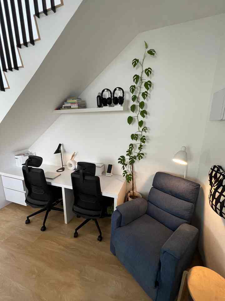 Monotone home office space featuring white desks, black office chairs, and a blue armchair cozy corner