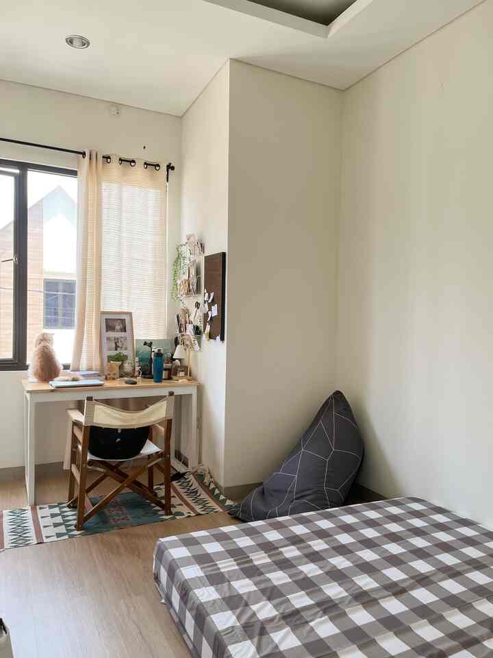 Beige and wood tone small bedroom and home office with desk and chair by window, and bean bag in the corner creating a cozy space