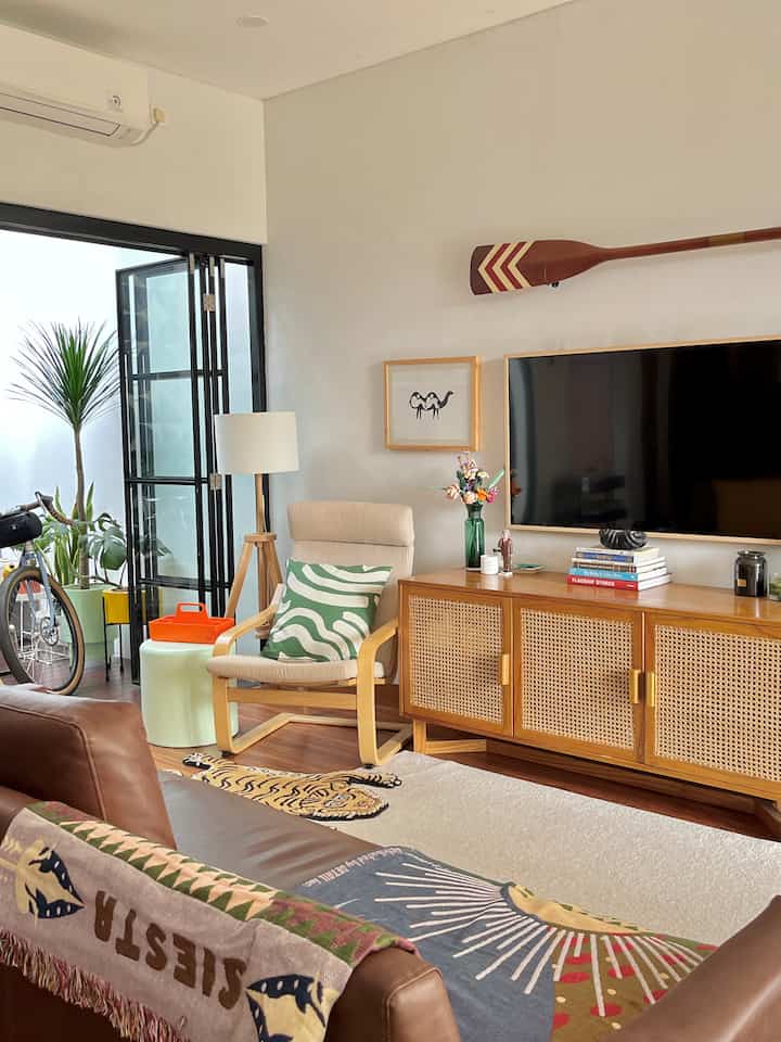 Natural tone living room featuring wood tone furniture, brown sofa, and armchair arranged for cozy atmosphere