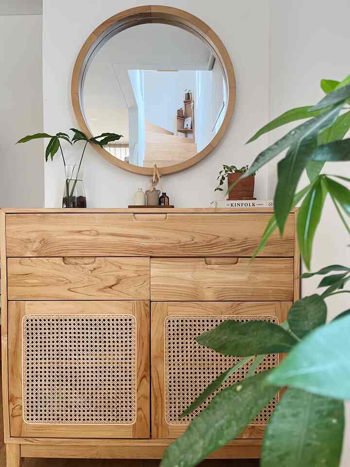 Natural wood tone entrance featuring a rattan cabinet, round mirror, and plants creating a warm, inviting atmosphere