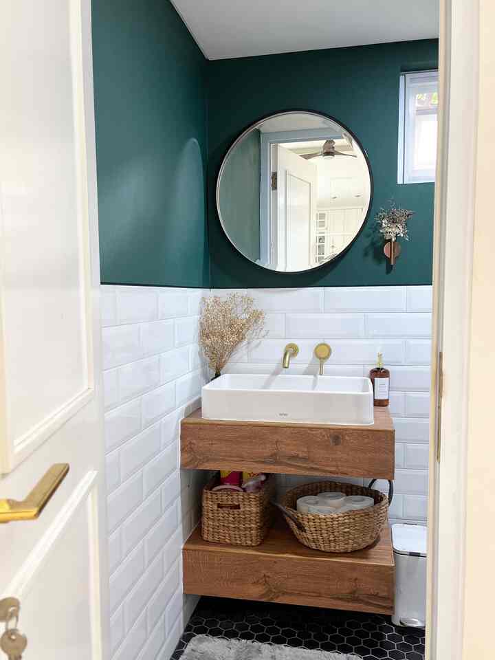 Compact powder room with white tiles, dark green walls, and wood-tone storage vanity