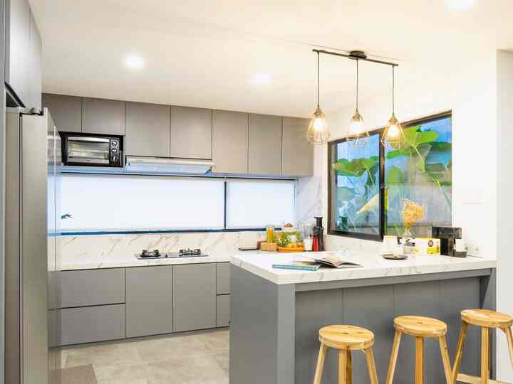 A modern kitchen in gray and white tones featuring a kitchen island, wooden stools, and pendant lighting creating a cozy atmosphere.