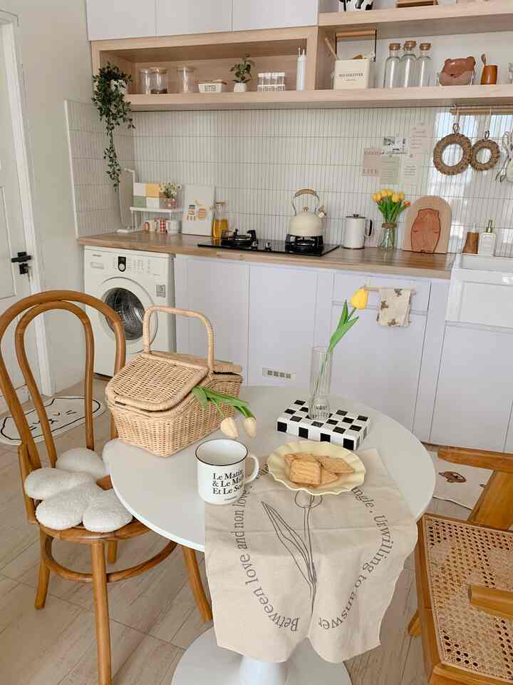 White and wood-tone cafe style kitchen featuring a round dining table, wooden chairs, small vase with tulip, and a cozy atmosphere