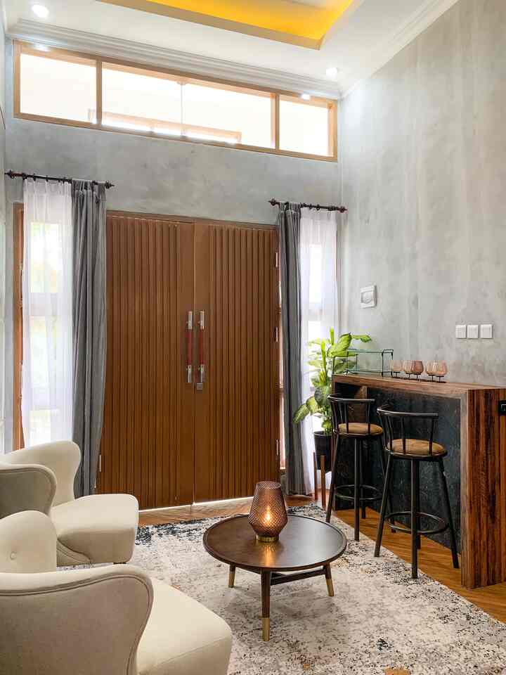 Natural brown tone living room featuring white armchairs, a round coffee table, and a wooden bar counter with bar stools creating a cozy home cafe space