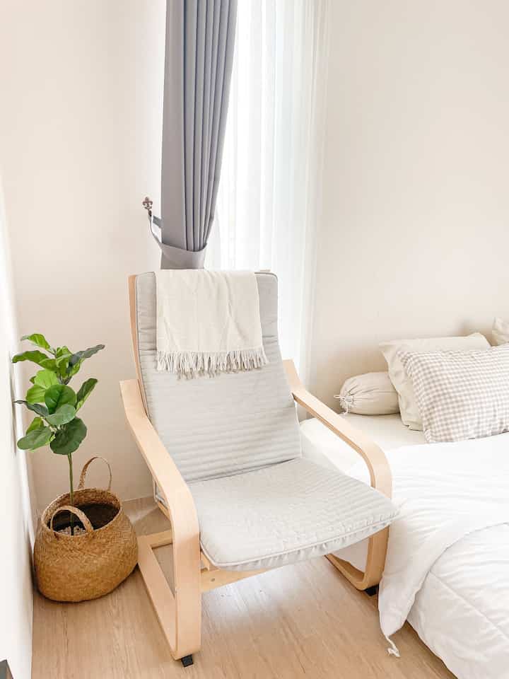 Natural-toned bedroom corner featuring wood armchair with beige cushion and rattan basket, creating a cozy relaxation spot