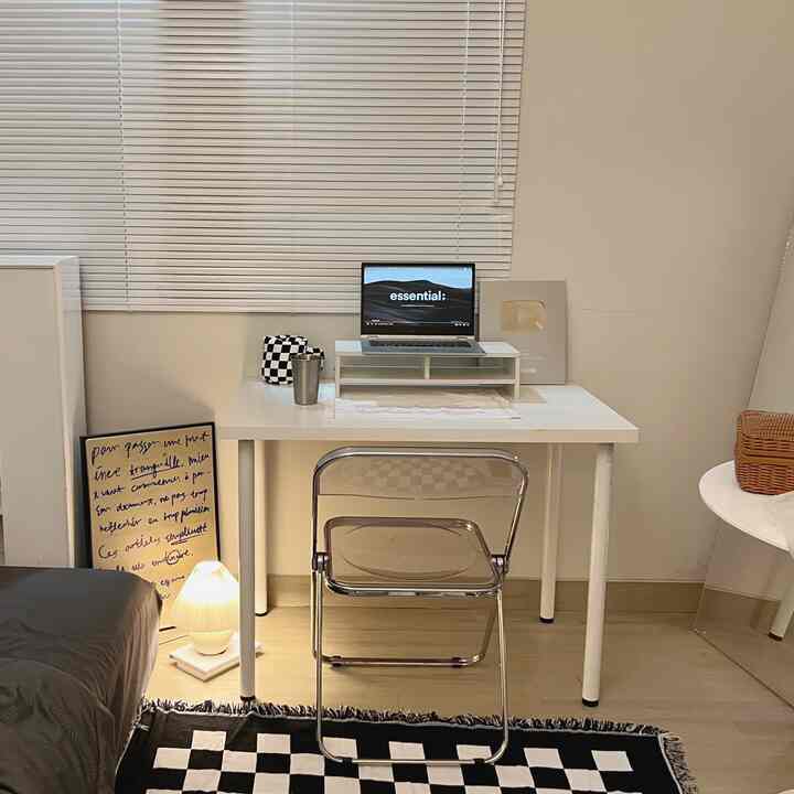 A cozy small bedroom home office in white and black monotone featuring a transparent chair and sleek white desk