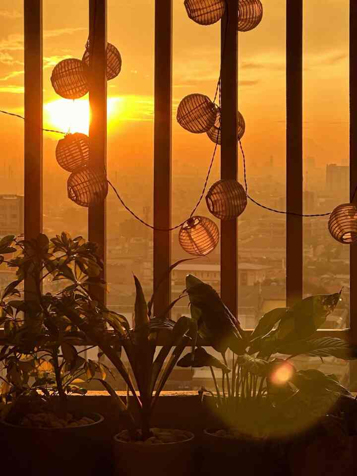 Gold-toned balcony featuring string lights and plants with a warm sunset atmosphere