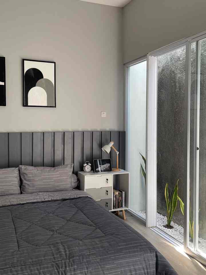 Modern bedroom in gray and white tones featuring a large bed with gray bedding and a small white nightstand with lamp