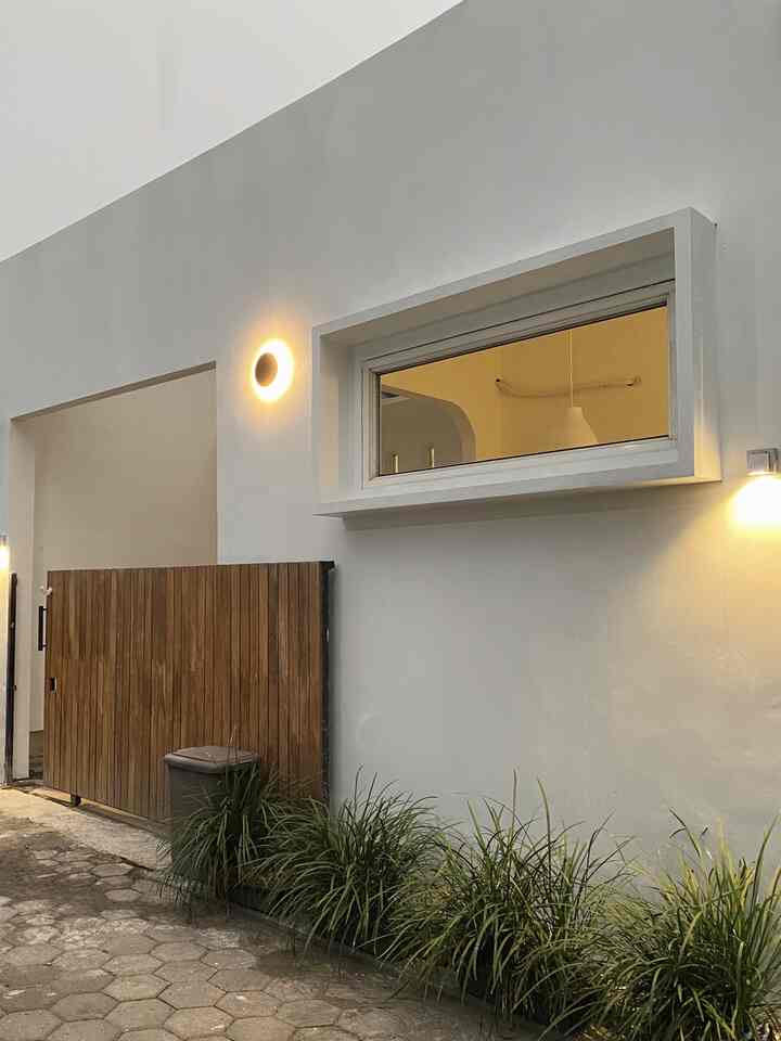 Minimalist entrance facade with dominant white walls and wood tone gate, featuring wall sconces creating a warm atmosphere