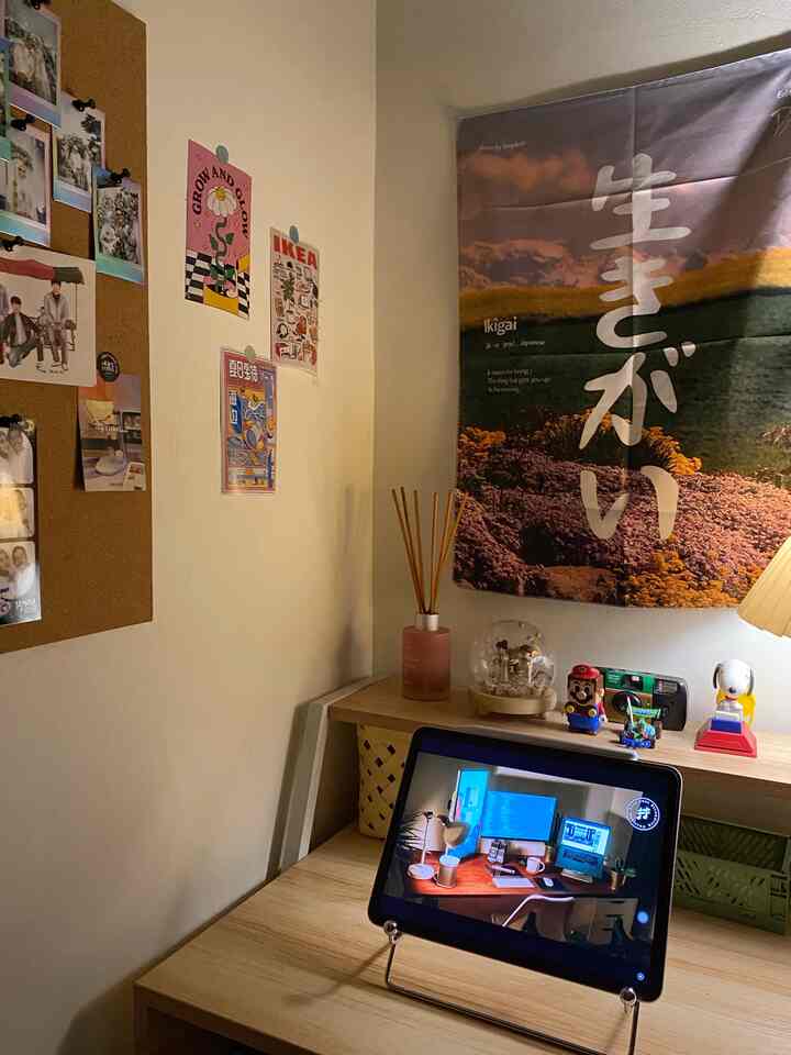 Warm-tone bedroom workspace featuring a natural wood desk, diffuser, Japanese language poster, and action figures creating a cozy atmosphere