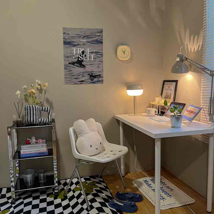 White and beige toned home office space featuring a simple desk, chair, poster, and soft lighting creating cozy ambiance