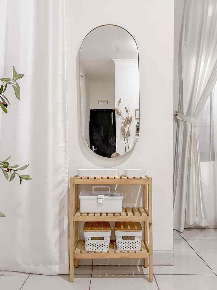 Corner space with white walls and wood tone shelving features a large mirror and small plant, creating a simple and natural atmosphere.