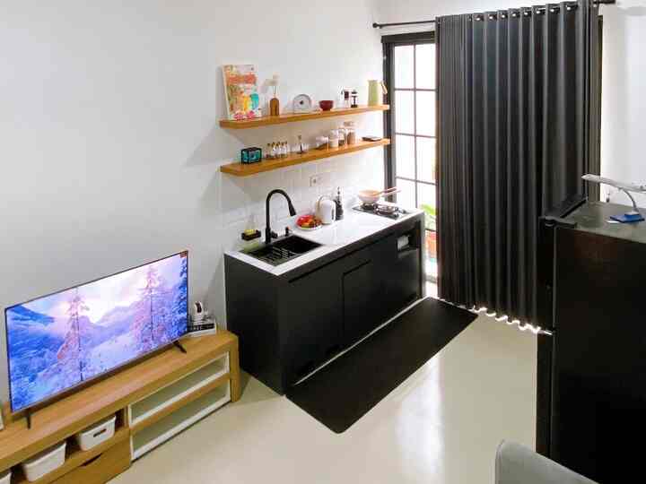 Modern small kitchen and living space featuring white walls and black kitchen cabinetry with wood-toned furniture