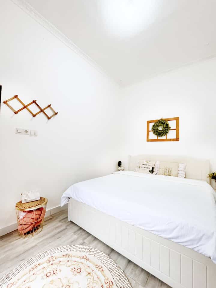 Small bedroom in white and wood tones featuring king-size bed, two nightstands, and round carpet with a simple cozy atmosphere