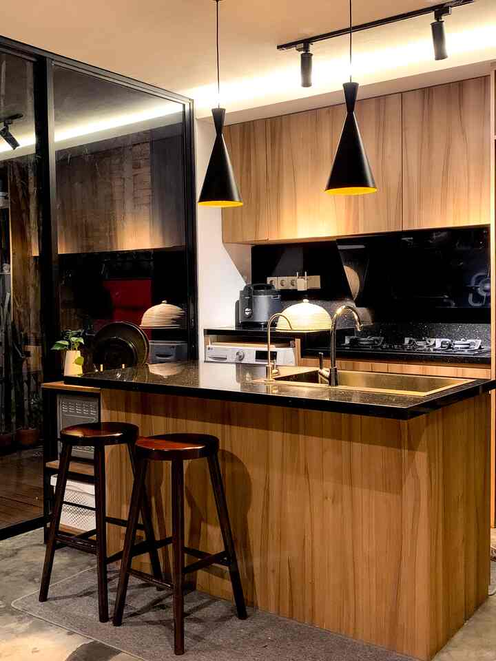 Modern kitchen in wood tone and black, featuring a kitchen island and pendant lights centered in a neat layout