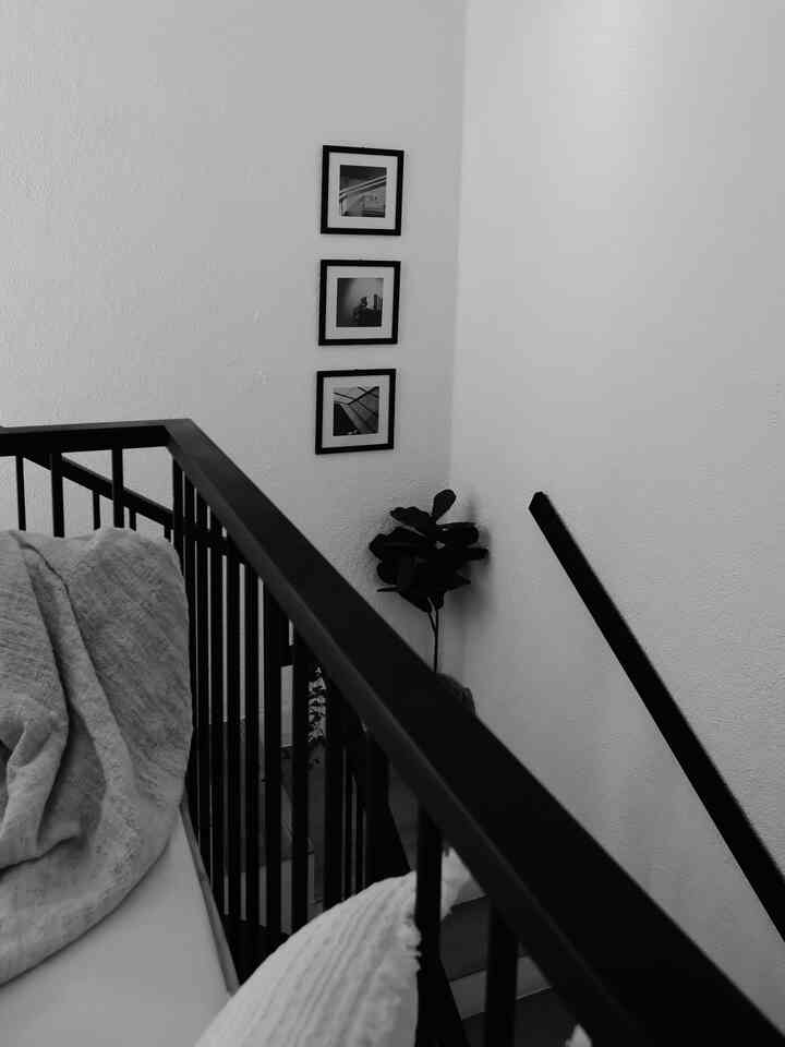 Modern stair area featuring white walls, black stair railing, and vertically arranged picture frames in corner