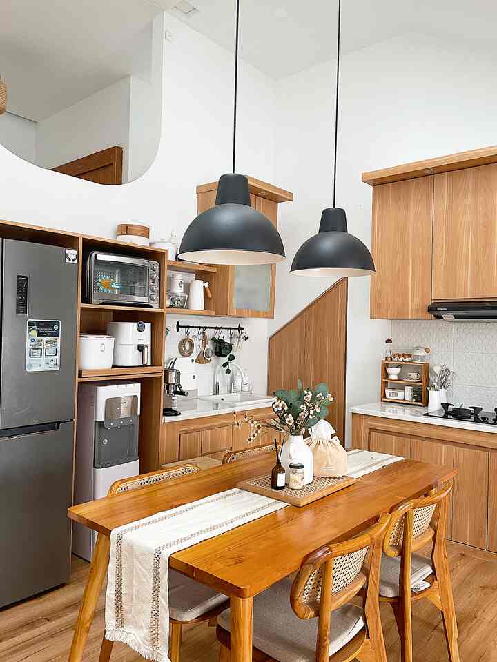 A warm wood tone and white combined dining room and kitchen featuring wooden dining table and chairs, pendant lights, table runner, and a vase creating a cozy atmosphere
