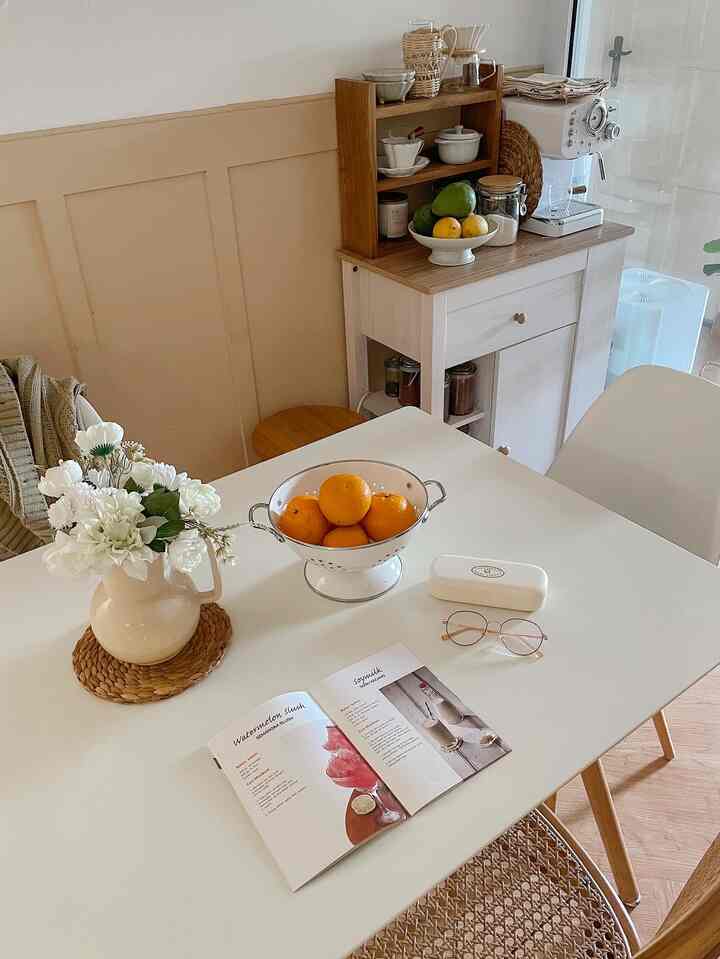 White and wood tone dining room featuring a dining table with oranges and a flower vase, creating a cozy atmosphere