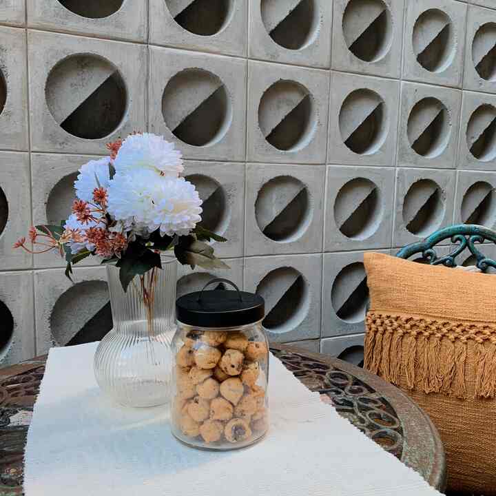 A white and transparent toned balcony featuring a clear glass vase and cookie jar, with an orange cushion creating a cozy atmosphere.