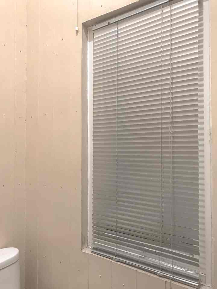 Corner of a bathroom space with beige walls and white blinds installed, clean and simple atmosphere