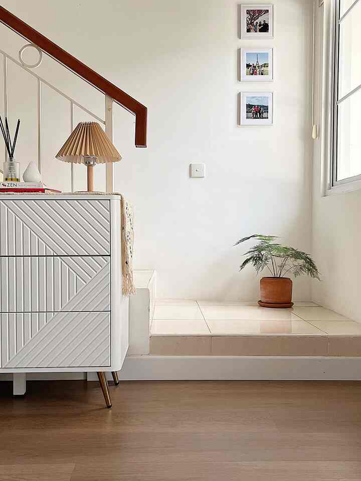 White and brown toned corner space featuring a storage dresser, table lamp, and terracotta plant pot with a tidy, cozy atmosphere