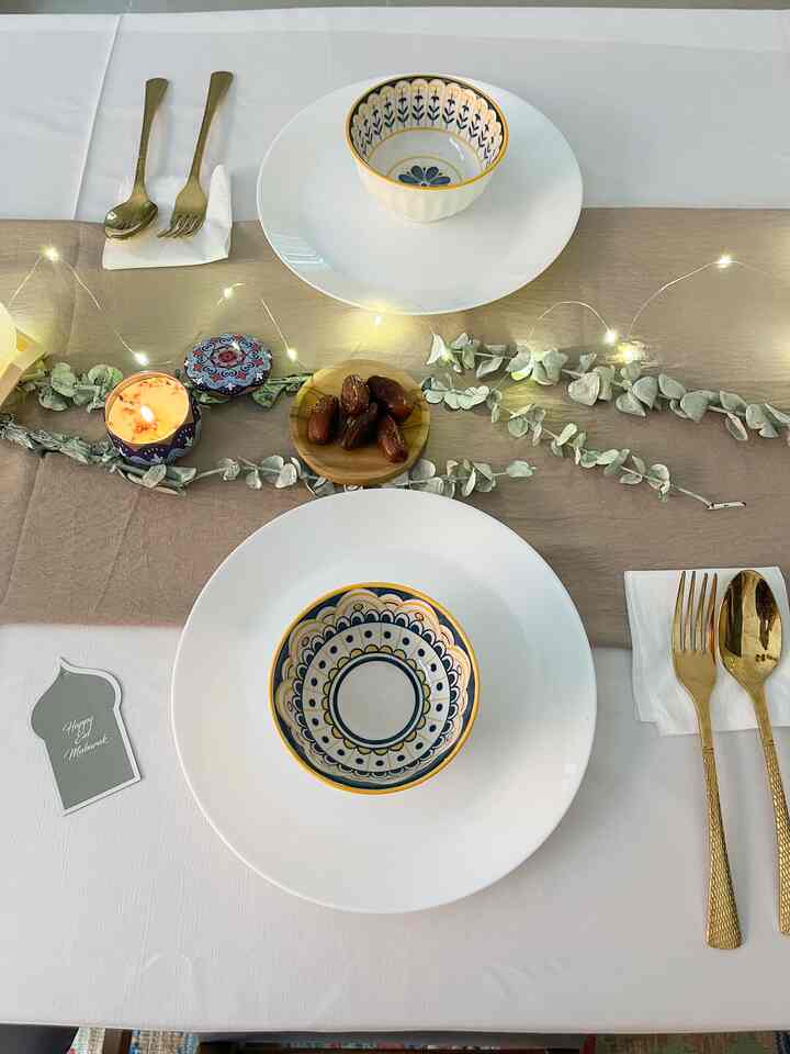 White and beige toned dining room featuring gold cutlery, Japanese tableware, candle, and eucalyptus decorations on an intimate Eid table setting